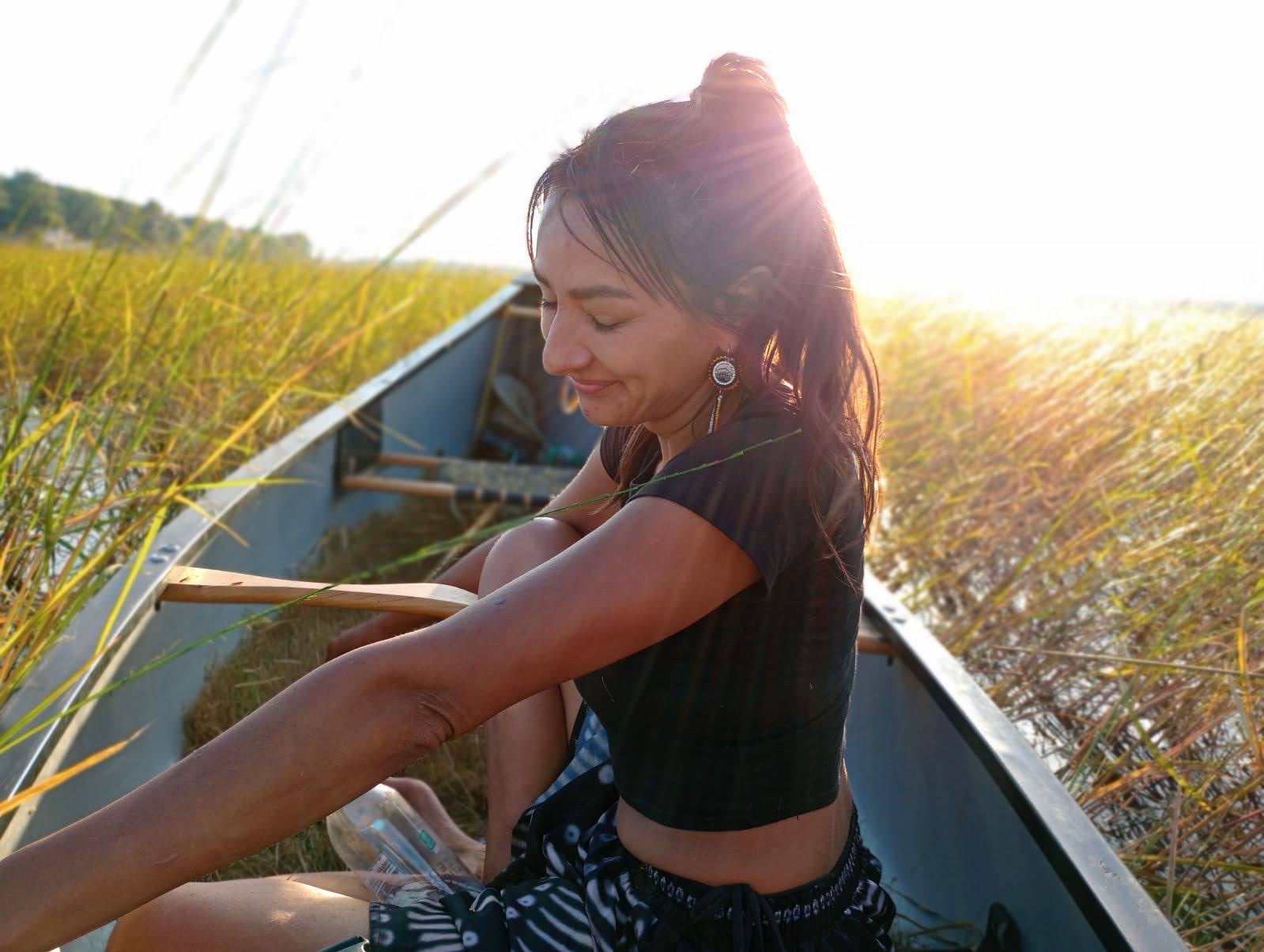 photo of an indigenous woman in a dark skirt and top in a canoe on a body of water full of rice plants