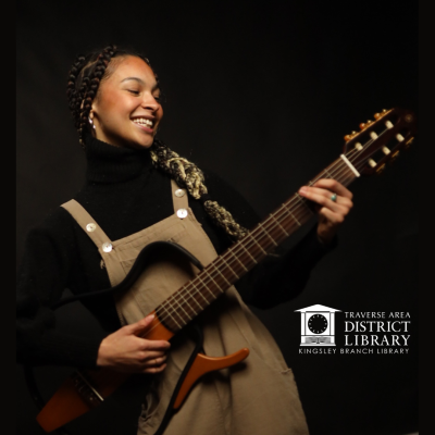 Image of the singer and songwriter SkyeLea Martin playing a guitar in front of a black background.