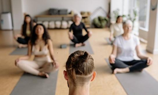 Photo of a yoga class. Students are sitting in the lotus position.