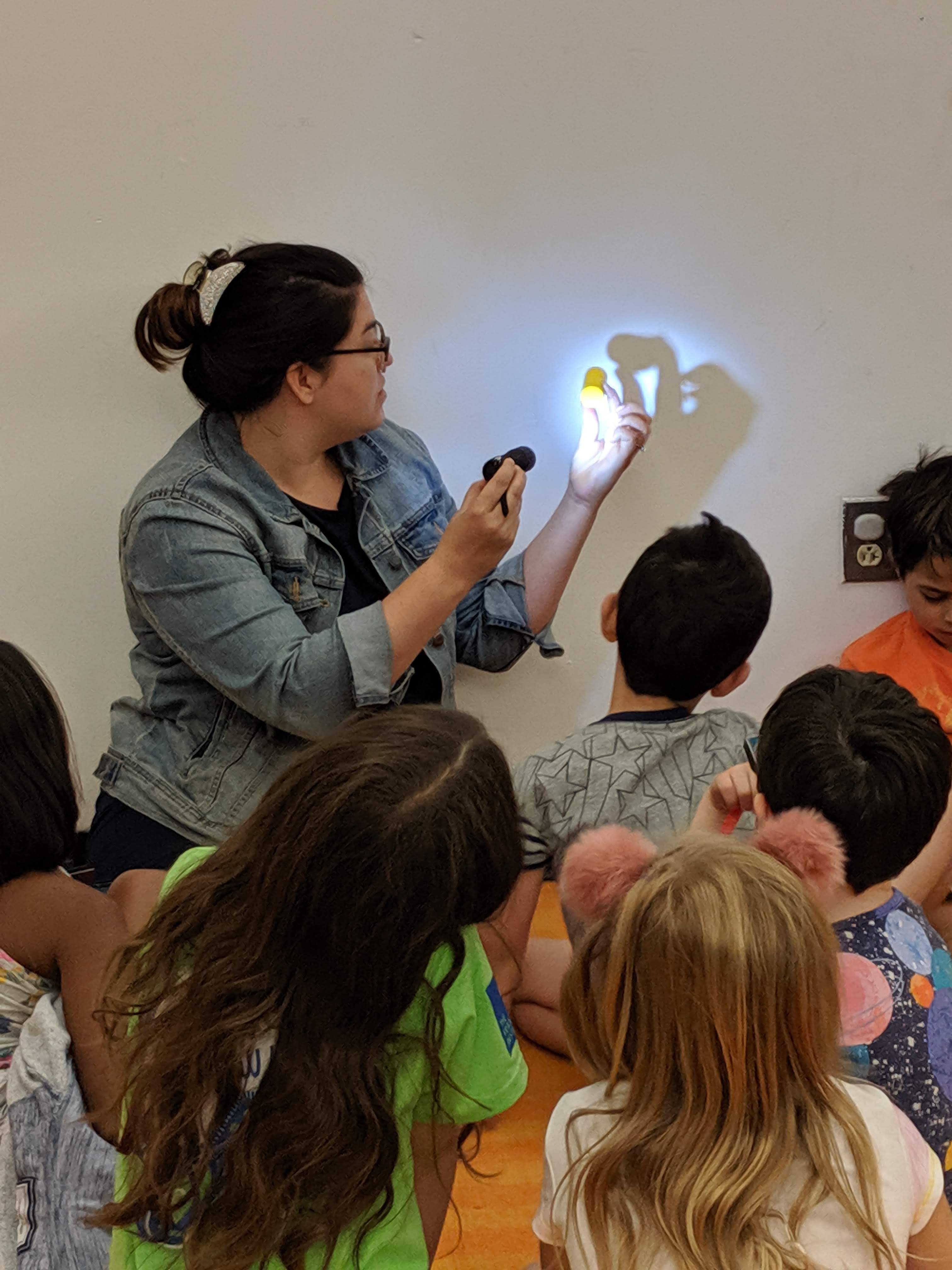 Preschool instructor demonstrating how to make a shadow using a flashlight and toy.