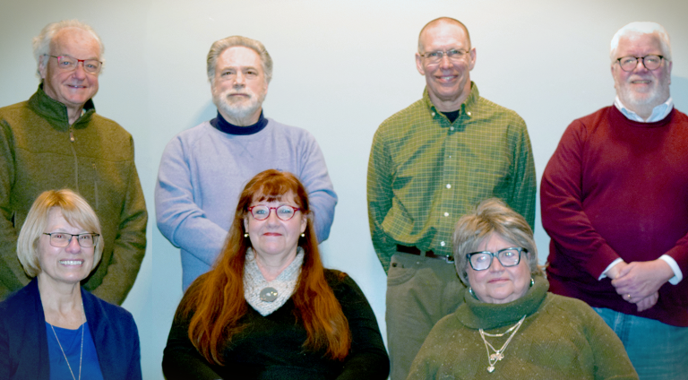 Four men standing in the back row, left to right are Michael Vickery, Joseph Jones, Paul Deyo, and Jeffrey Wescott. The three female members of the board are seated in the front row. Left to right they include Marylee Pakieser, Susan Odgers, and Carol Sullivan.