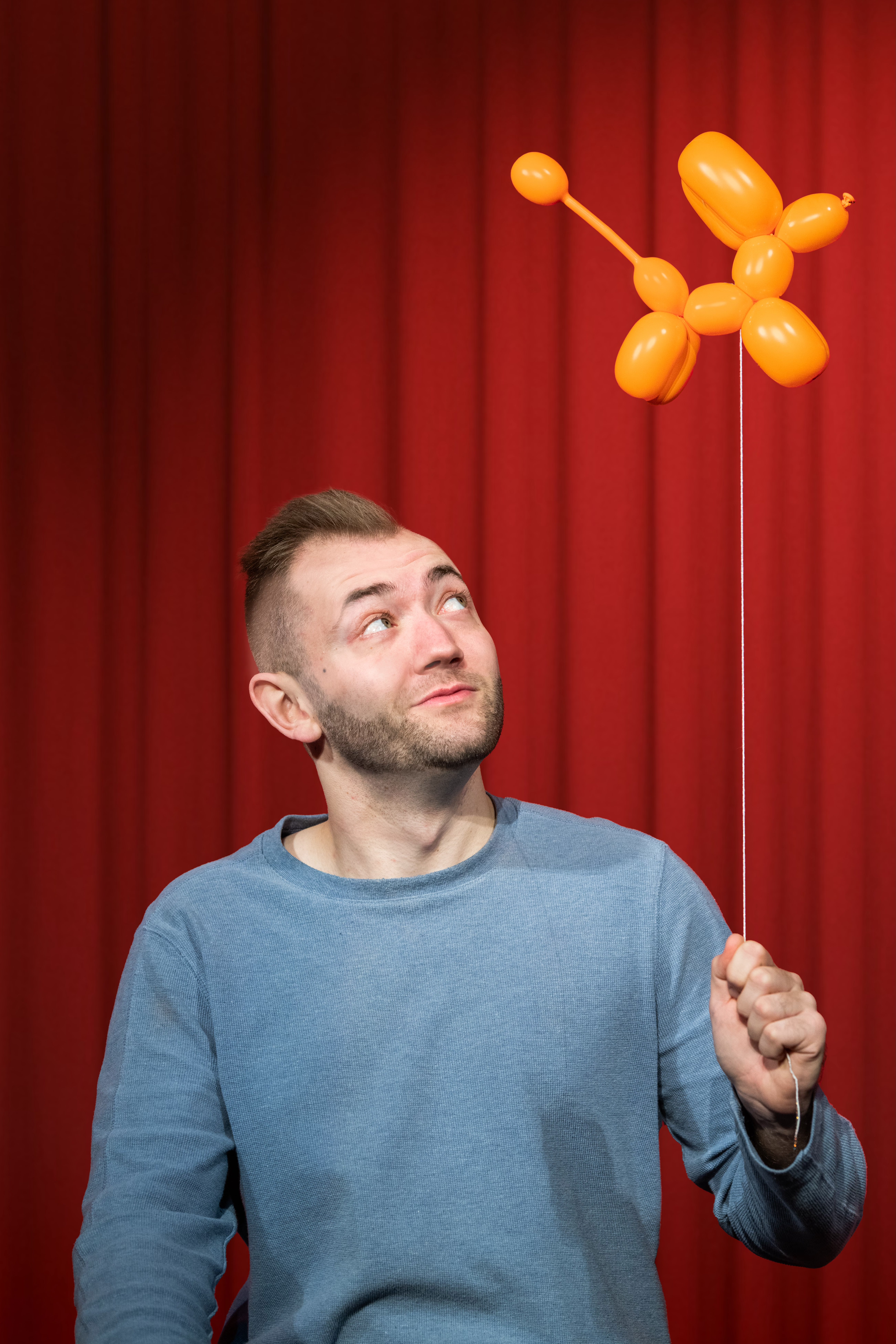 Image of magician Zvara in a blue sweater with a dog balloon animal fling above him.