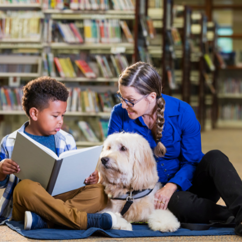 Children reading book to therapy dog with doghandler present