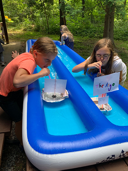 children around a blue inflatable pool floating toy boats