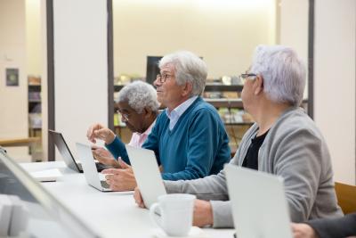 Photograph of 3 senior citizens all sitting at a table in front of laptops