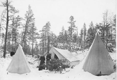 Image of two people standing outside a of a snow-covered tent. Image in black and white, appears to be from the 1870s.